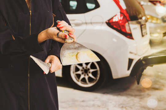 Preparation for car repair work : Hands female auto painter holding lamp and putty mixture used to smooth gaps in car surface for repainting in a full service auto repair service center. 