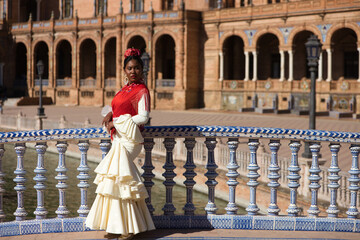 Young black woman dressed as a flamenco gypsy in a square in Seville, Spain. She wears a beige...