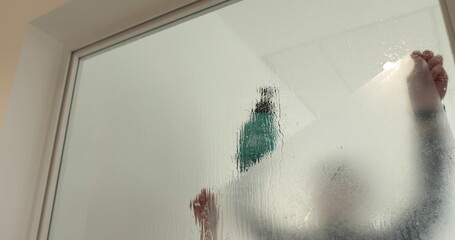 A man pastes a frosted coating on a glass door in a clinic to make the glass door opaque. Applying a matte coating to the glass.