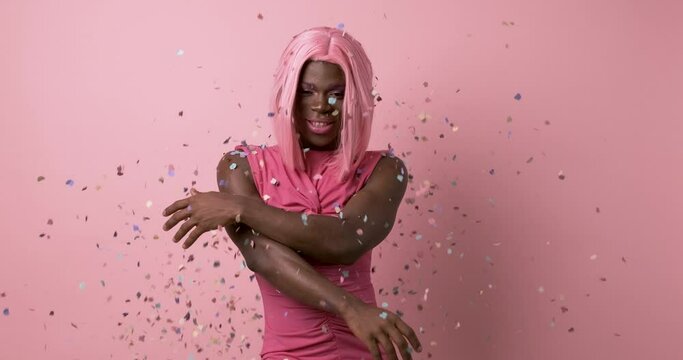 Cheerful black transgender throwing confetti in air against pink background