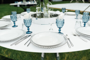 Open -air wedding banquet. The table is decorated with white plates and premium glasses for wine