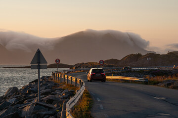 sunset over lofoten, with fog coming in, road with car driving away, road signs