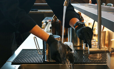 A coffee shop worker is using his hands to clean pitcher stainless steel.