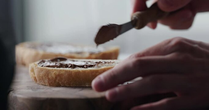 Slow motion man spread chocolate nut cream on ciabatta slice