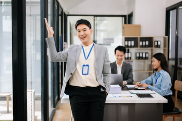 Fototapeta premium Young attractive Asian male office worker business suits smiling at camera with working notepad, tablet and laptop documents in office