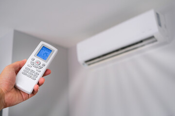 Man's hand using remote control open The air conditioner is cooled to 25 degrees Celsius in his...