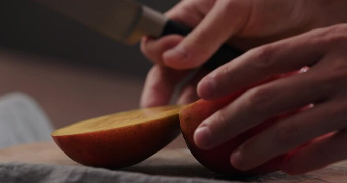 Slow motion man cut ripe red mango on olive wood board