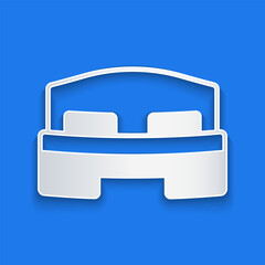 Paper cut Hotel room bed icon isolated on blue background. Paper art style. Vector