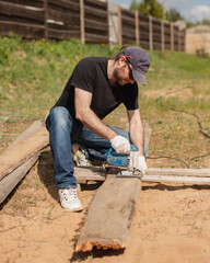 A man builds and paints a fence from rough boards - rustic processing style - summer warm day