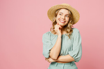 Young smiling happy woman she wear summer casual clothes straw hat put hand prop up on chin, lost in thought and conjectures isolated on plain pastel light pink background studio. Lifestyle concept.