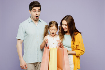 Young shocked surprised parents mom dad with child daughter girl 6 years old in blue yellow casual clothes hold shopping package bag isolated on plain purple background Black Friday sale day concept