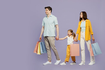 Fototapeta premium Full body side view young happy parents mom dad with child daughter girl 6 years old wear yellow casual clothes hold shopping bags go isolated on plain purple background Black Friday sale day concept