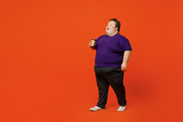Fototapeta na wymiar Full size body side view young chubby overweight man wear purple t-shirt casual clothes hold takeaway delivery craft brown cup coffee to go isolated on plain red orange background. Lifestyle concept.