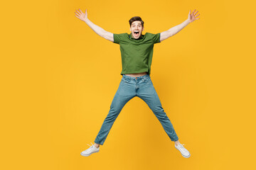 Full body young overjoyed excited cool fun happy man he wears green t-shirt casual clothes jump high with outstretched hands legs isolated on plain yellow background studio portrait Lifestyle concept