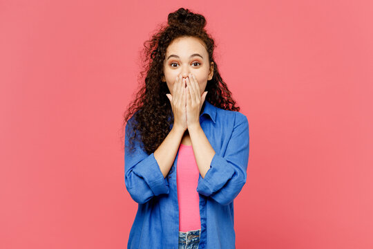 Young shocked surprised fun woman of African American ethnicity she wear blue shirt casual clothes cover mouth with hand look camera isolated on plain pastel pink background studio. Lifestyle concept.
