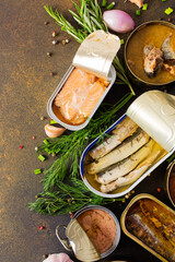 Different open tin cans with canned fish among spices and herbs on a brown background, canned...