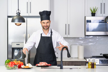 Handsome man is preparing food in kitchen. Handsome mature middle-aged man cooking meat in kitchen. Man preparing food meal in kitchen. Healthy food and cooking in kitchen concept.
