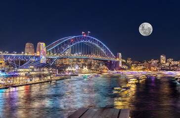Panoramic night view of Sydney Harbour and City Skyline with a Sturgeon full Moon NSW Australia bright neon lights reflecting off the water