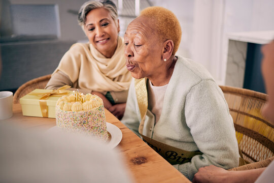 Senior woman blowing candles on her cake for birthday celebration at a house at a party with friends. Smile, happy and elderly female person with a dessert to celebrate with people in retirement home