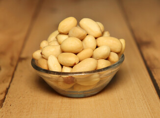 Peanut (groundnut and goober) in wooden bowl, used as a snack. Isolated macro food photo wooden background, side close up. 