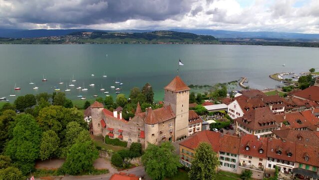 Aerial view of Murten castle and old town with red roofs on Lake Murten shore, Switzerland. Scenic medieval architecture in Canton Fribourg, historic fortification and blue lakeside, drone 4k video.
