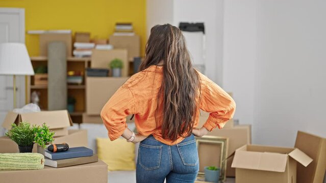 Young beautiful hispanic woman looking around standing backwards at new home