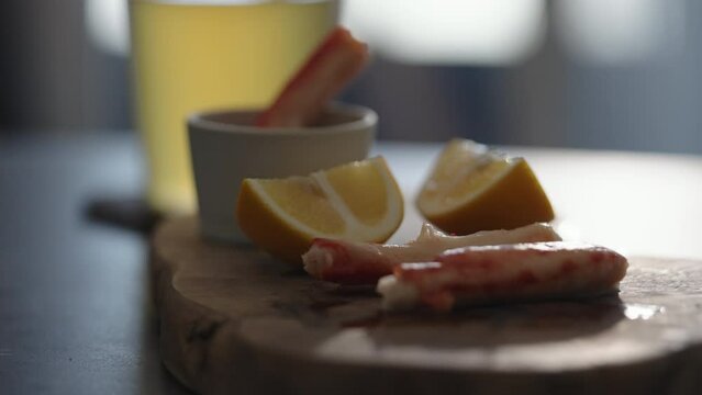 Slow motion gimbal shot of crab leg meat on a olive board with sweet lemon and dip sauce on concrete countertop
