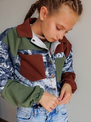 A little girl with blond long hair in two pigtails buttons up a demi-season jacket for a product demonstration