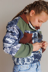 A little girl with blond long hair in two pigtails buttons up a demi-season jacket for a product demonstration