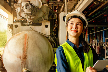 Asian female technician worker in engineering department wearing hard hat supervising machinery...