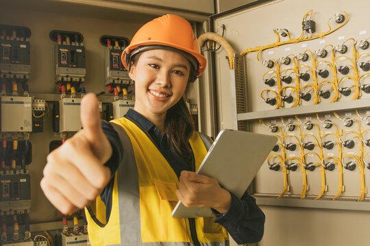 Engineer electrician confident female worker showing thumbs up checking machine control cabinet three phase electrical system using 380 volts electricity with frequent tripping main breaker problem.