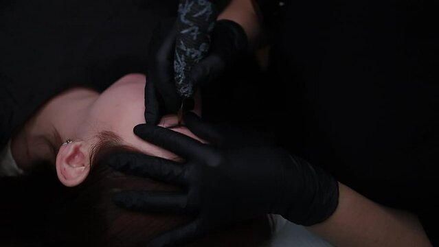 The permanent make-up master holds the models eyebrow and applies permanent makeup.