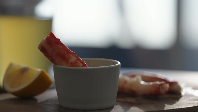 Slow motion gimbal shot of crab leg meat on a olive board with sweet lemon and dip sauce on concrete countertop