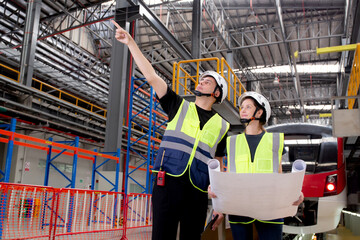 Young caucasian engineer man and woman or worker looking blueprint and checking electric train for planning maintenance in station, transport and infrastructure, inspector check service transport.
