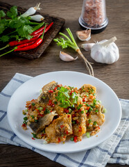 Deep-fried sea bass in salt and pepper in a white plate on a wooden table