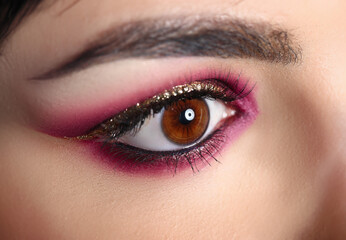 Close-up of model charming eye. Professional makeup in burgundy colors with golden glitters. Perfect eyebrow shape. Art of evening maquillage. Beauty and cosmetics concept