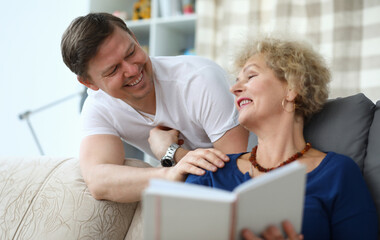 Elderly woman reads book at home, next adult son. Home quarantine upon contact with patient. Strict rules self-isolation. Contact person to contact for help. Home food supply parent