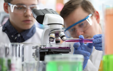 Man pours liquid into test tube under microscope. Production methods drugs are constantly being...