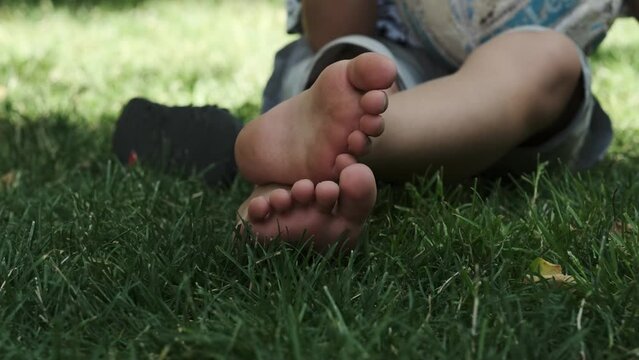 The legs of a teenager sitting barefoot on the grass in a park on a sunny day.