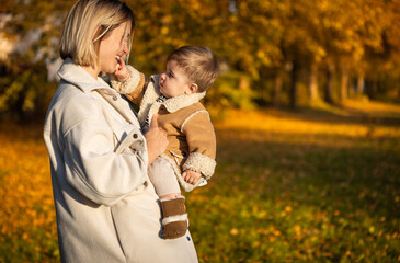 Fototapeta premium Mother holding baby boy on hands walking autumn park