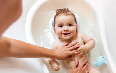 Mom bathing her smiling baby in bathtub