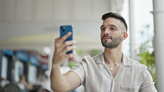 Young hispanic man smiling confident making selfie by the smartphone at coffee shop terrace