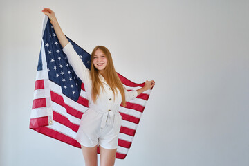 Girl holds the American flag on a light background. Independence Day concept. A woman celebrates a national holiday