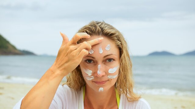 Close-up portrait woman apply sun cream protection lotion. Cute woman near sea on beach smearing sunscreen cream in style war paint. Seductive girl looking at camera. Person applying sunscreen cream