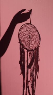 a dreamcatcher shadow on pink wall. Dreamcatcher in silhouette of a woman's hand on a pink background.