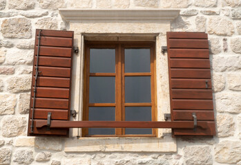 Traditional brown wooden open window shutters on stone wall