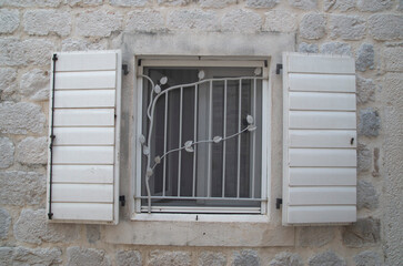 Traditional white woodeTraditional white wooden open window shutters and metal grill with floral ornaments in Europen open window shutters on stone home