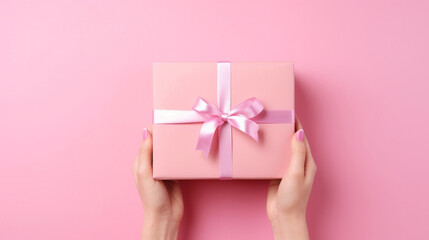 Hands of a girl with a manicure holding a gift box with a bow on a pink background