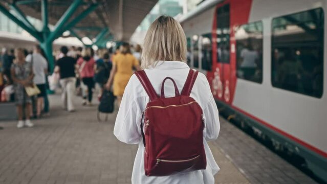 A woman at the train station walks on a platform next to commuter trains. Daily use of public transport in urban life.