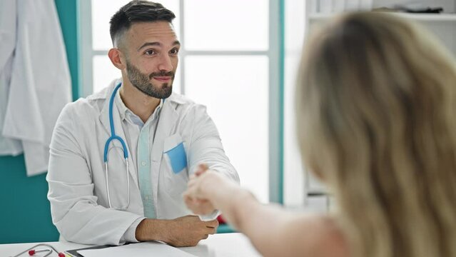Young hispanic man doctor shaking hands with patient at the clinic